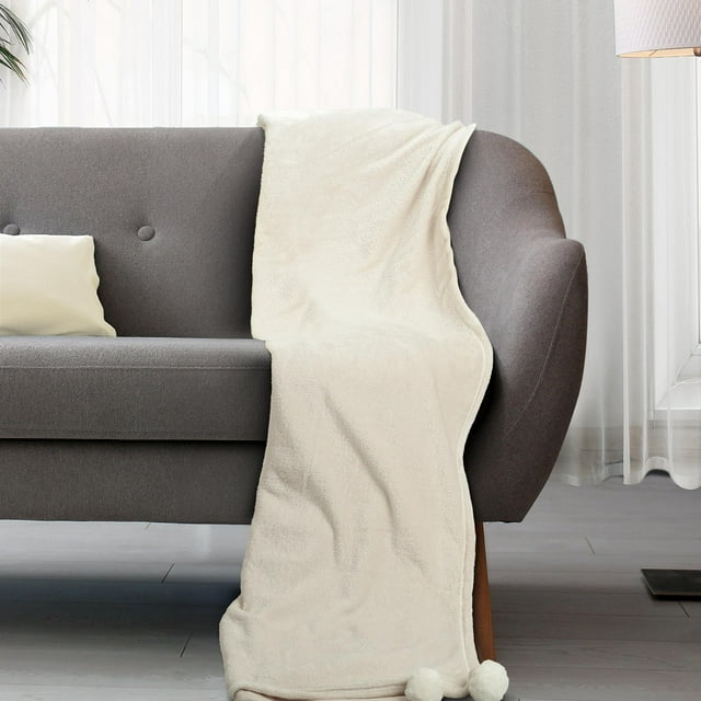 Cream colored throw blanket with pom poms on the corners